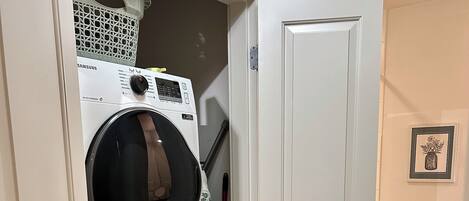 A laundry room with stacked washers and dryers, a broom, and a toilet visible through an open door.