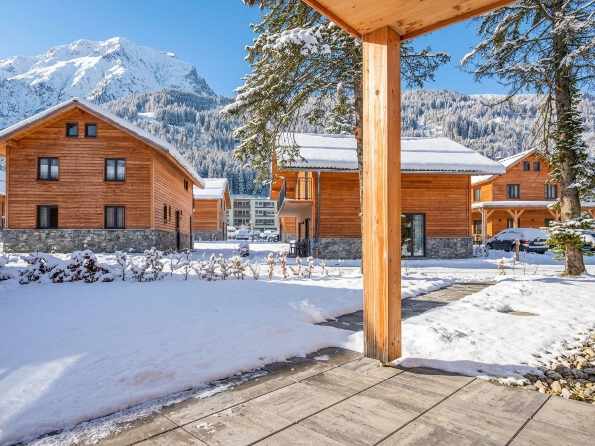 A wooden cabin with a stone foundation, surrounded by snow-covered ground and trees, with a mountain in the background.