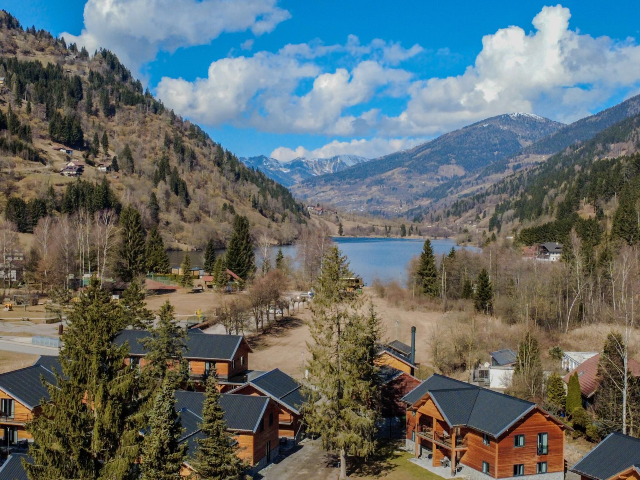 A mountainous landscape with a lake, wooden cabins, and a clear sky.