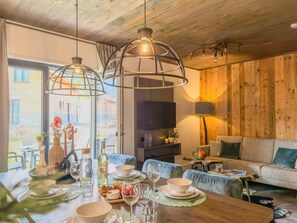 Un comedor con una mesa de madera lista para una comida, un sofá y un televisor al fondo.