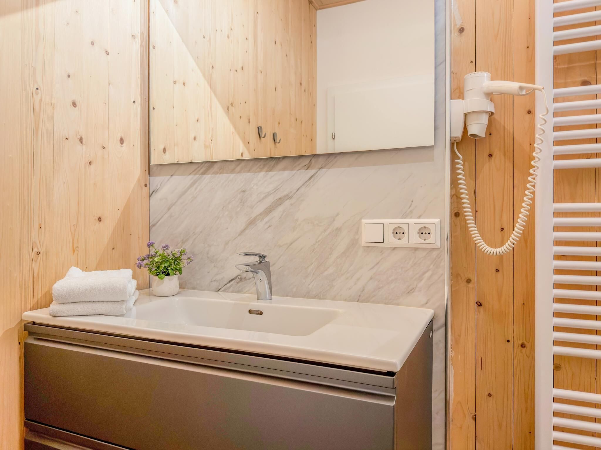 A bathroom with a wooden wall, a marble backsplash, a sink with a faucet, a towel, a potted plant, and a telephone.