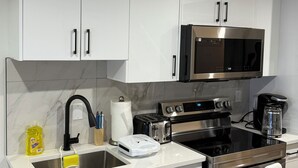 Una cocina moderna con armarios blancos, un microondas de acero inoxidable, un tostador, una cafetera y un horno Samsung.