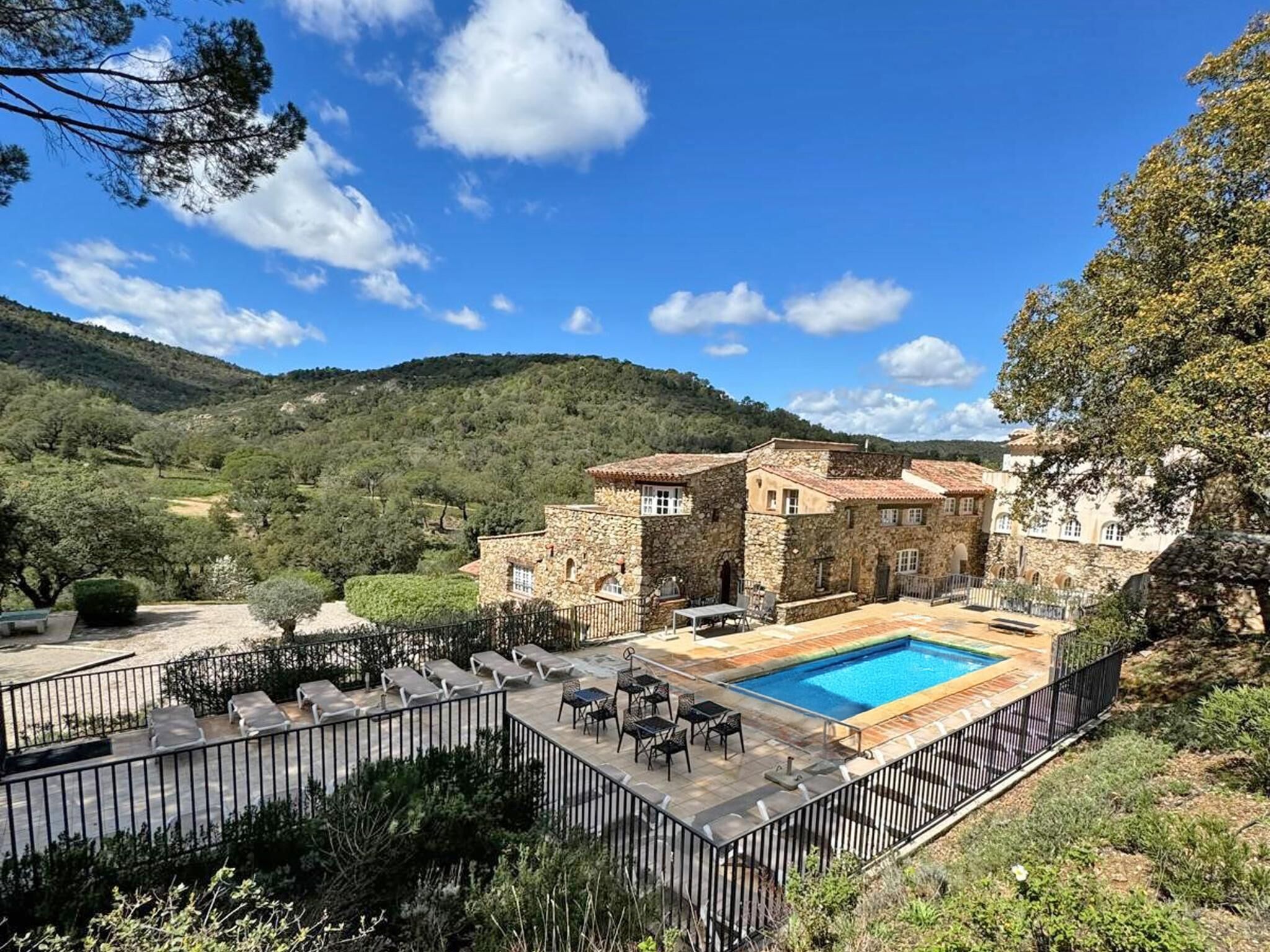 Una villa de piedra con piscina, mobiliario exterior y montañas al fondo.