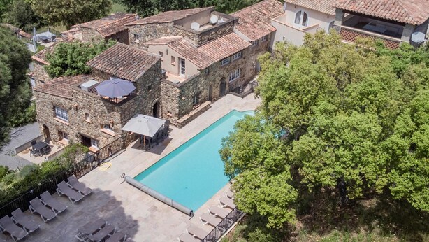 Um edifício de pedra tradicional com piscina, rodeado por vegetação exuberante.