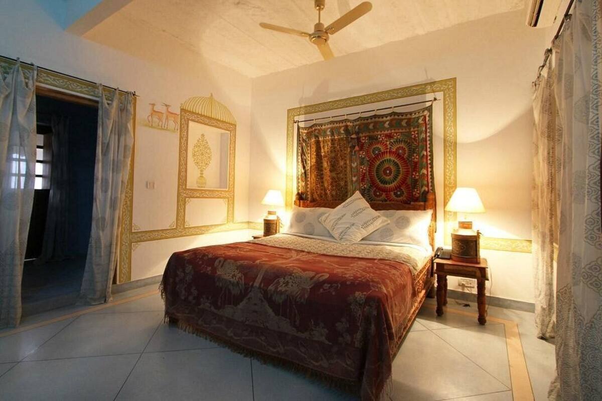 A bedroom with a large bed, two bedside tables, a ceiling fan, and a tapestry on the wall.