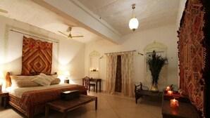 A spacious bedroom with a large bed, a wooden bench, a desk, and a chair. There are two lamps, a ceiling fan, and a decorative vase with candles. - Barsingha Villa (Bap)