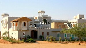 A large, multi-story building with a central courtyard, featuring a prominent archway and a small tower. - Barsingha Villa (Bap)