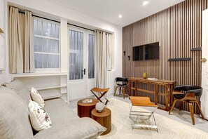 A modern living room with a sofa, coffee table, and TV wall mounted above a wooden panel wall. - TheBlueStay 99 - Apartment in the heart of Paris (Paris)