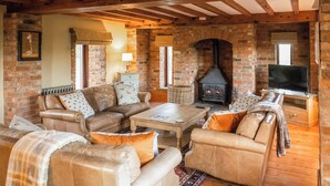 A cozy living room with a stone fireplace, leather sofas, a wooden coffee table, and a television on a wooden stand. - The Threshing Barn - UKC8847 (Blankney Fen)