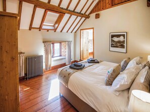 Un dormitorio con techo de madera, una cama grande con almohadas, un radiador y una ventana con cortinas.