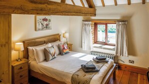 A wooden-framed bedroom with a bed, bedside tables, a window with curtains, and a radiator. - The Threshing Barn - UKC8847 (Blankney Fen)