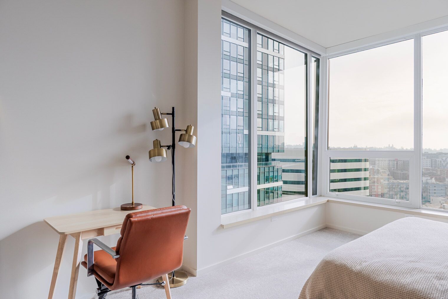 Ein modernes Hotelzimmer mit großem Fenster, Schreibtisch, Stuhl und Bett.