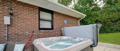 Jacuzzi frente a una casa de ladrillo con ventana y toma de corriente.