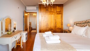 Ein Hotelzimmer mit einem großen Bett, einem Holzschrank, einem Schreibtisch mit Spiegel und einer Kandelaber.