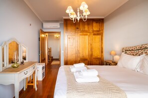 A hotel room with a large bed, wooden wardrobe, a desk with a mirror, and a chandelier. - GuestReady - Charming retreat in Funchal (Funchal)