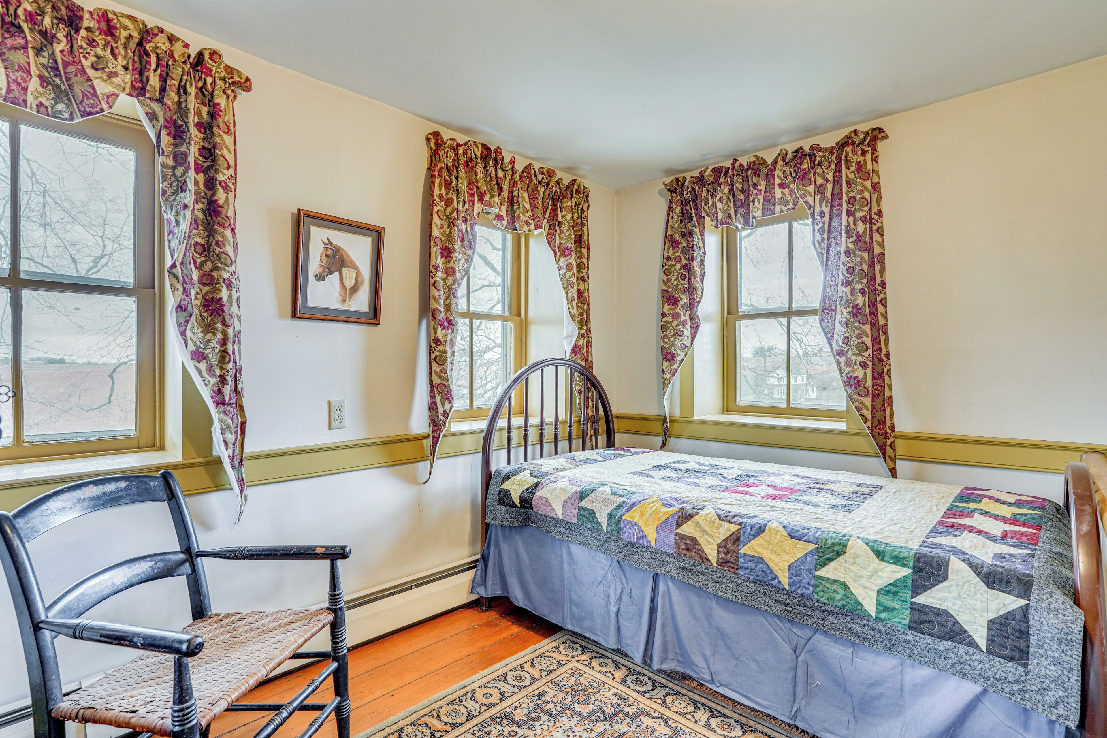 A bedroom with a bed, a chair, and two windows with curtains.