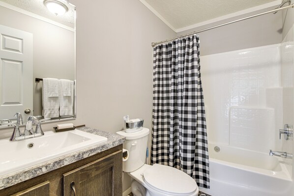 A bathroom with a white sink, toilet, and bathtub. There is a checkered shower curtain and a mirror above the sink. - Near State Park! Pet-Friendly Home in Crossville (Crossville)