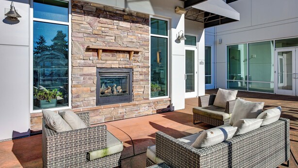 A modern outdoor living area with a stone fireplace, wicker furniture, and large windows offering views of the outdoors. - 4 Mi to Dtwn, Commuter-Friendly Apt in Tacoma (Tacoma)