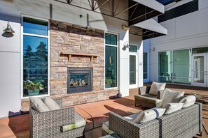 A modern outdoor living area with a stone fireplace, wicker furniture, and large windows offering views of the outdoors. - 4 Mi to Dtwn, Commuter-Friendly Apt in Tacoma (Tacoma)