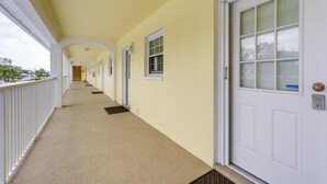 Un pasillo con una puerta blanca, una ventana con persianas y una barandilla blanca.