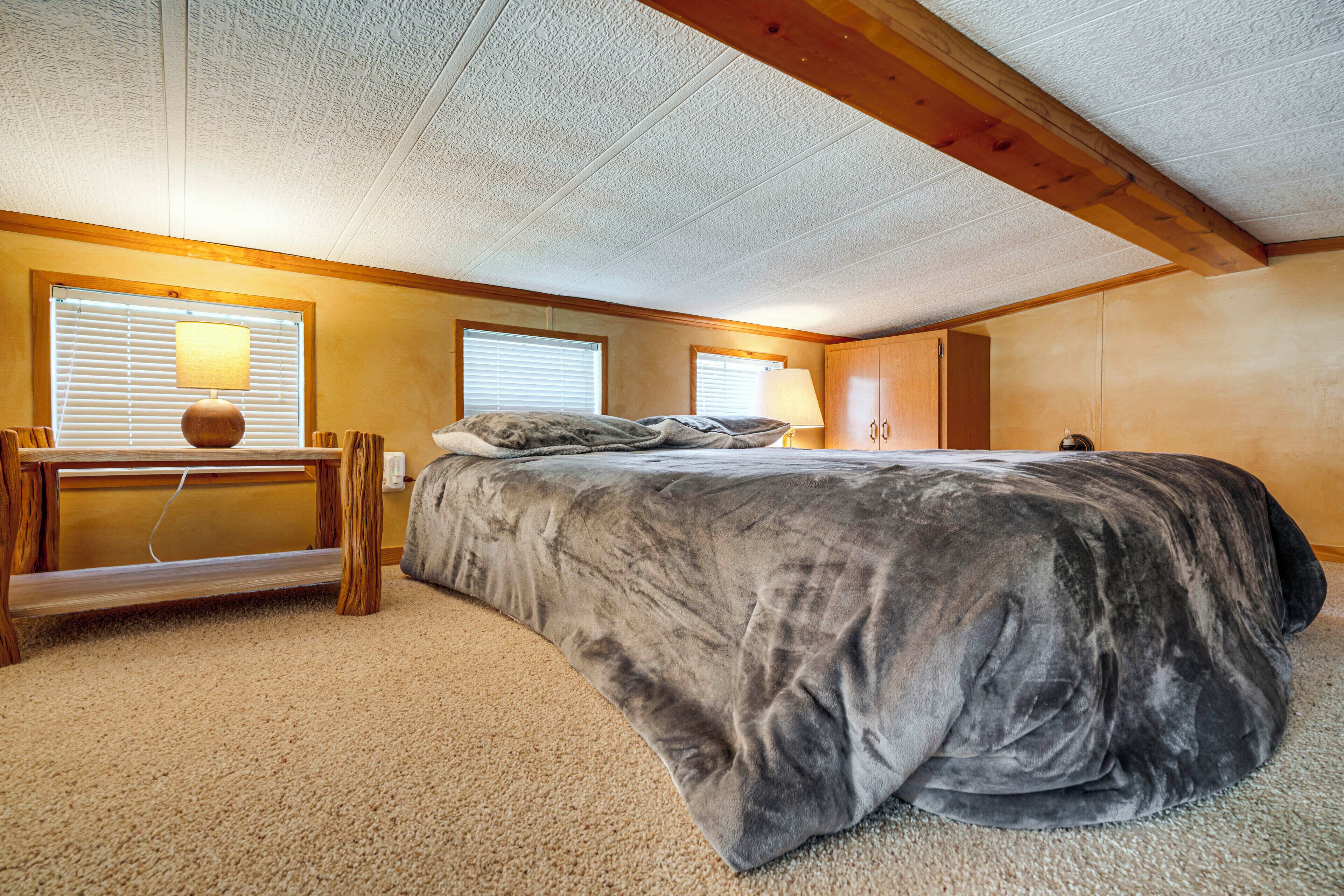 A bedroom with a large bed, wooden headboard, two bedside lamps, a wooden desk, and a window with blinds.