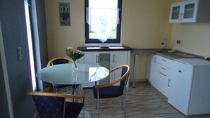 Eine kleine Küche mit Esstisch und Stühlen, einem Fenster mit Vorhang und einer Mikrowelle über der Arbeitsfläche.