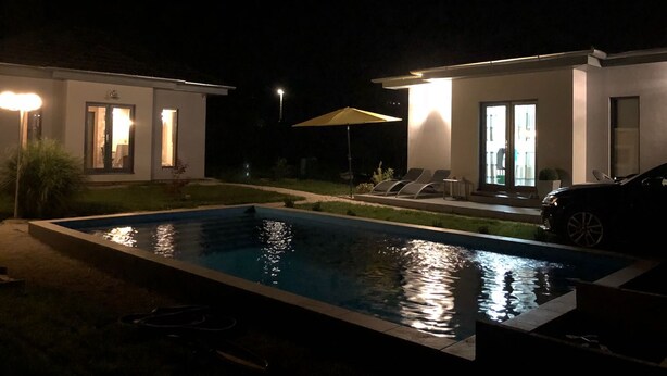Ein Nachtblick auf ein modernes Haus mit Schwimmbad, zwei Liegestühlen und einem in der Nähe geparkten Auto.
