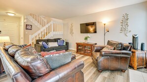 A living room with leather sofas, a staircase, a flat-screen TV, and a wooden cabinet. - Cozy Family Retreat! Home in Charlotte Suburbs (Charlotte)