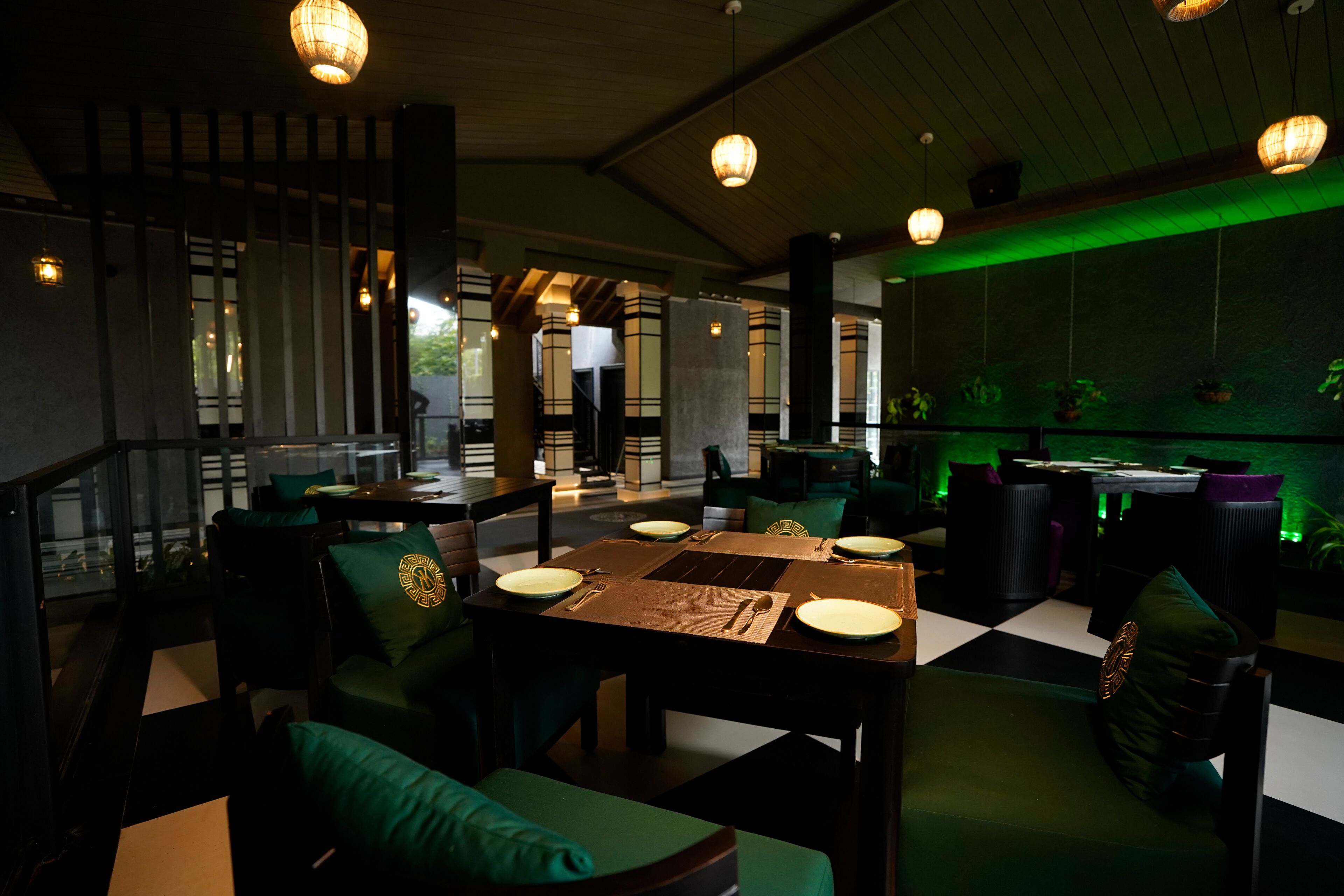 Un ristorante con pavimento a scacchi, sedie rivestite in verde e lampade a sospensione.