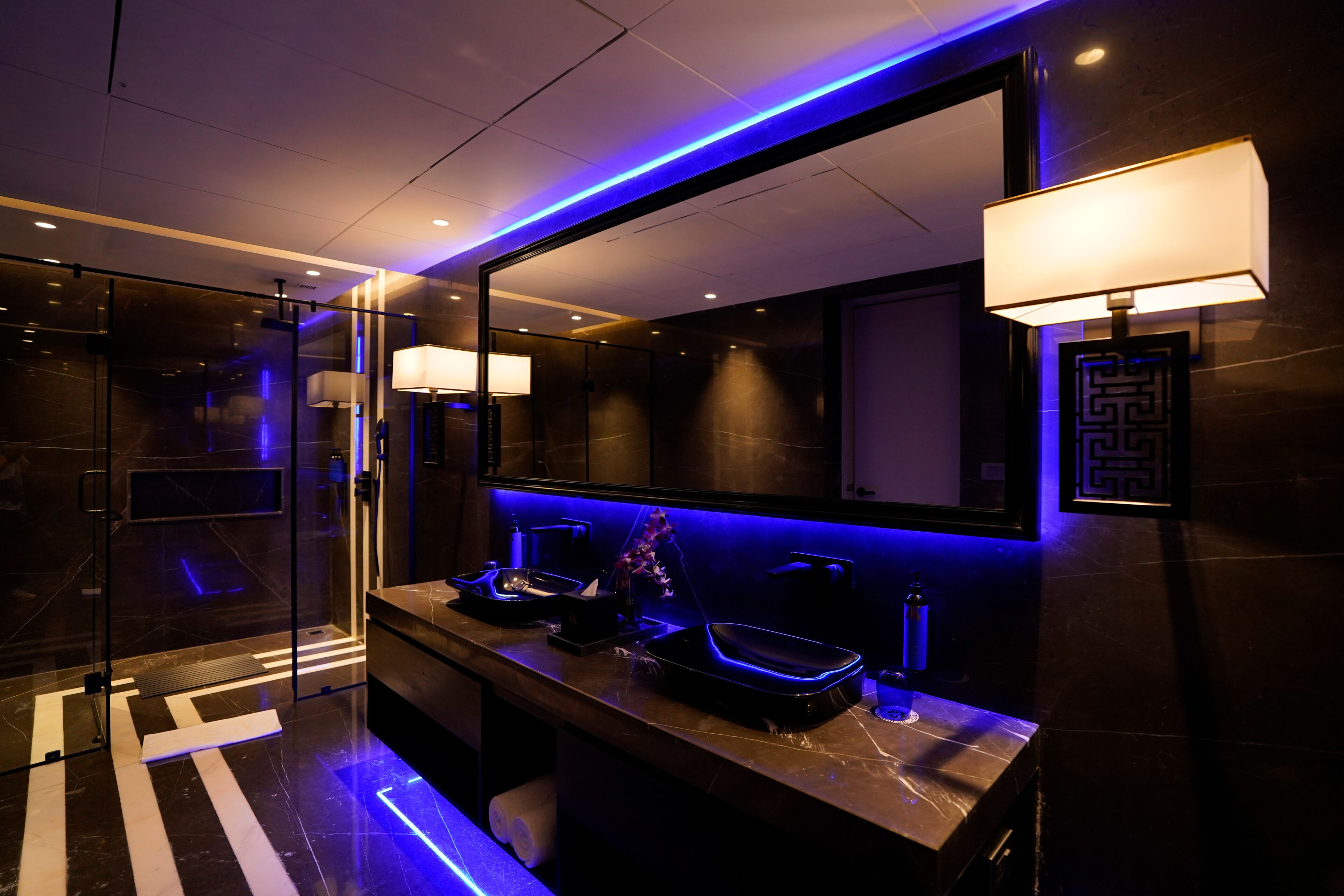 A modern bathroom with a glass shower enclosure, a vanity with a black sink, and a mirror with a light fixture above it.