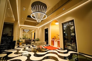 A hotel lobby with a modern design, featuring a large chandelier, a patterned floor, and a reception desk. - Kings Mansion (Candolim)