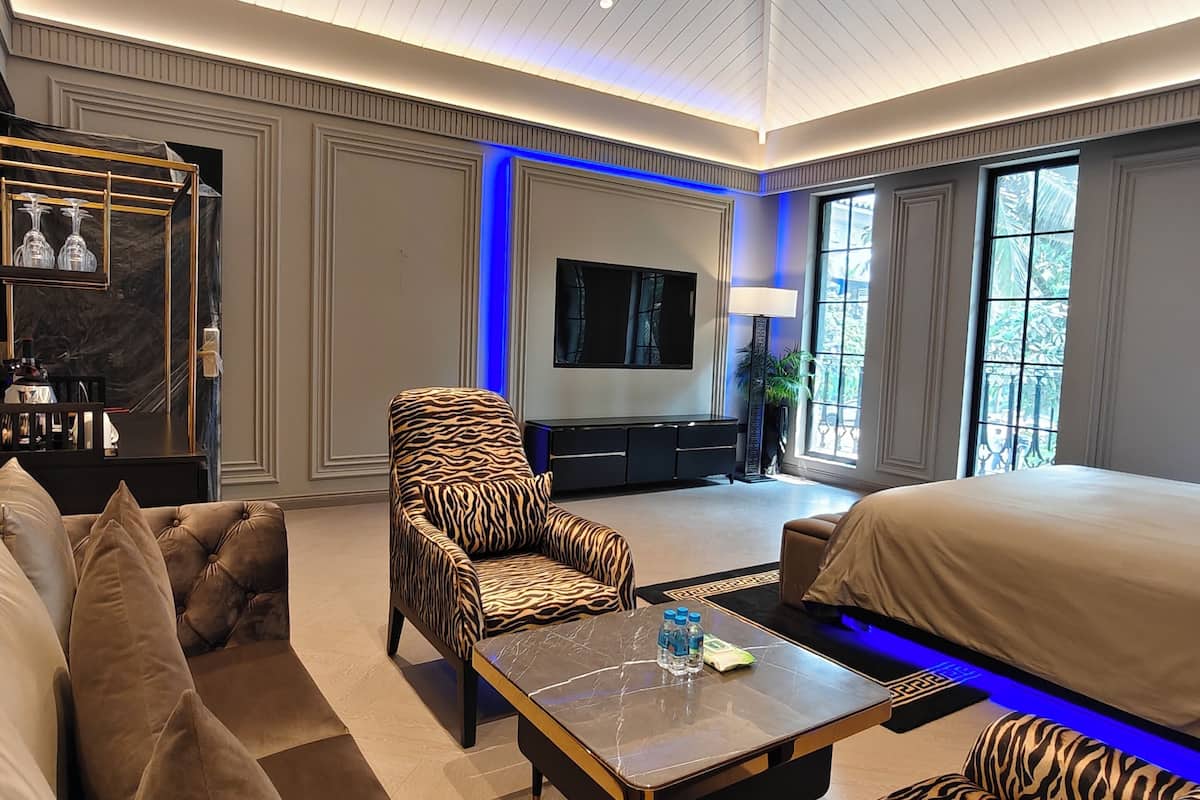 Ein geräumiges Wohnzimmer mit einem großen Flachbildfernseher, einer Couch, einem Sessel mit Zeprazmuster und einem Bett.
