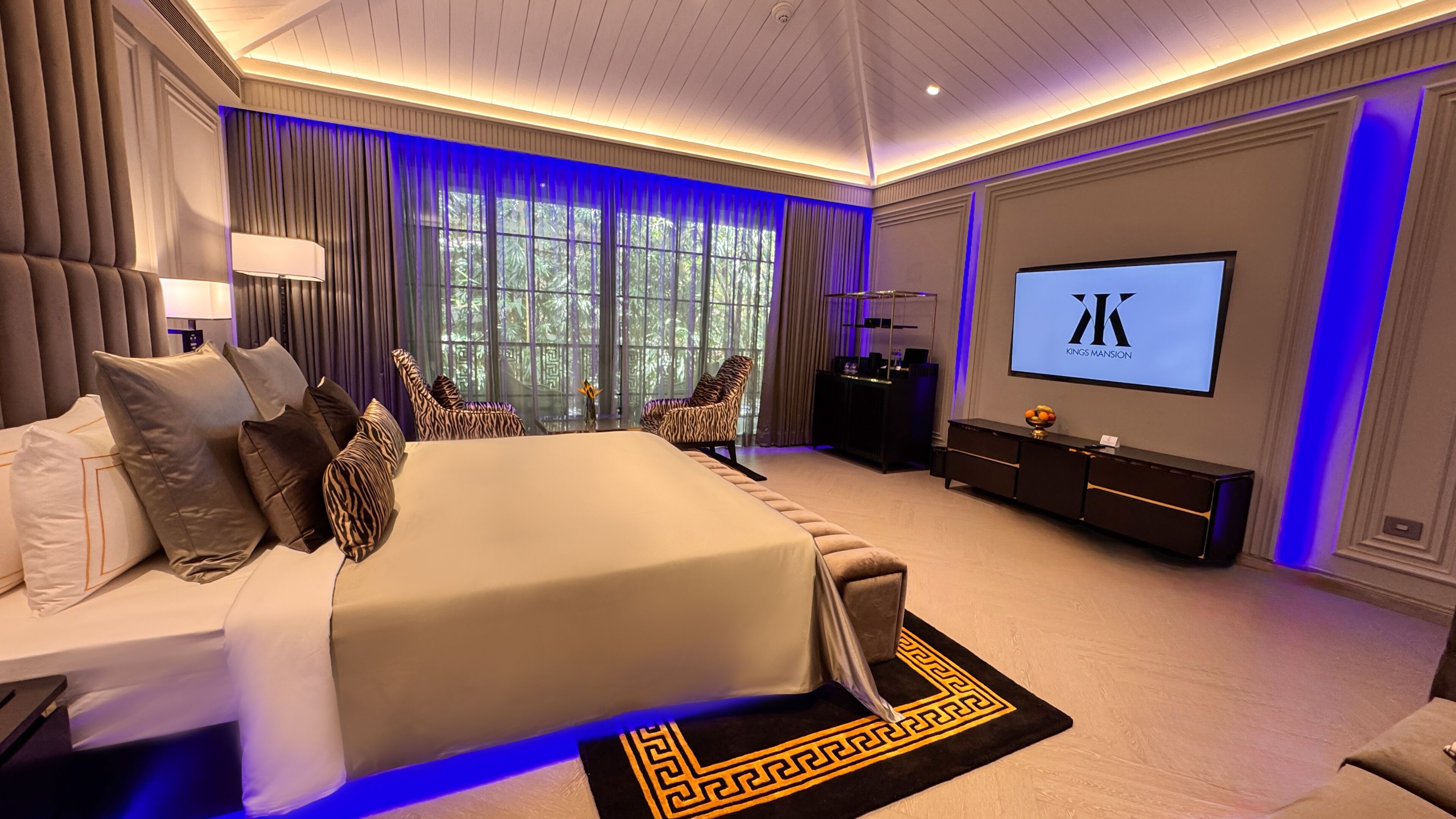 A spacious bedroom with a large bed, a TV, and a view of trees through the window.