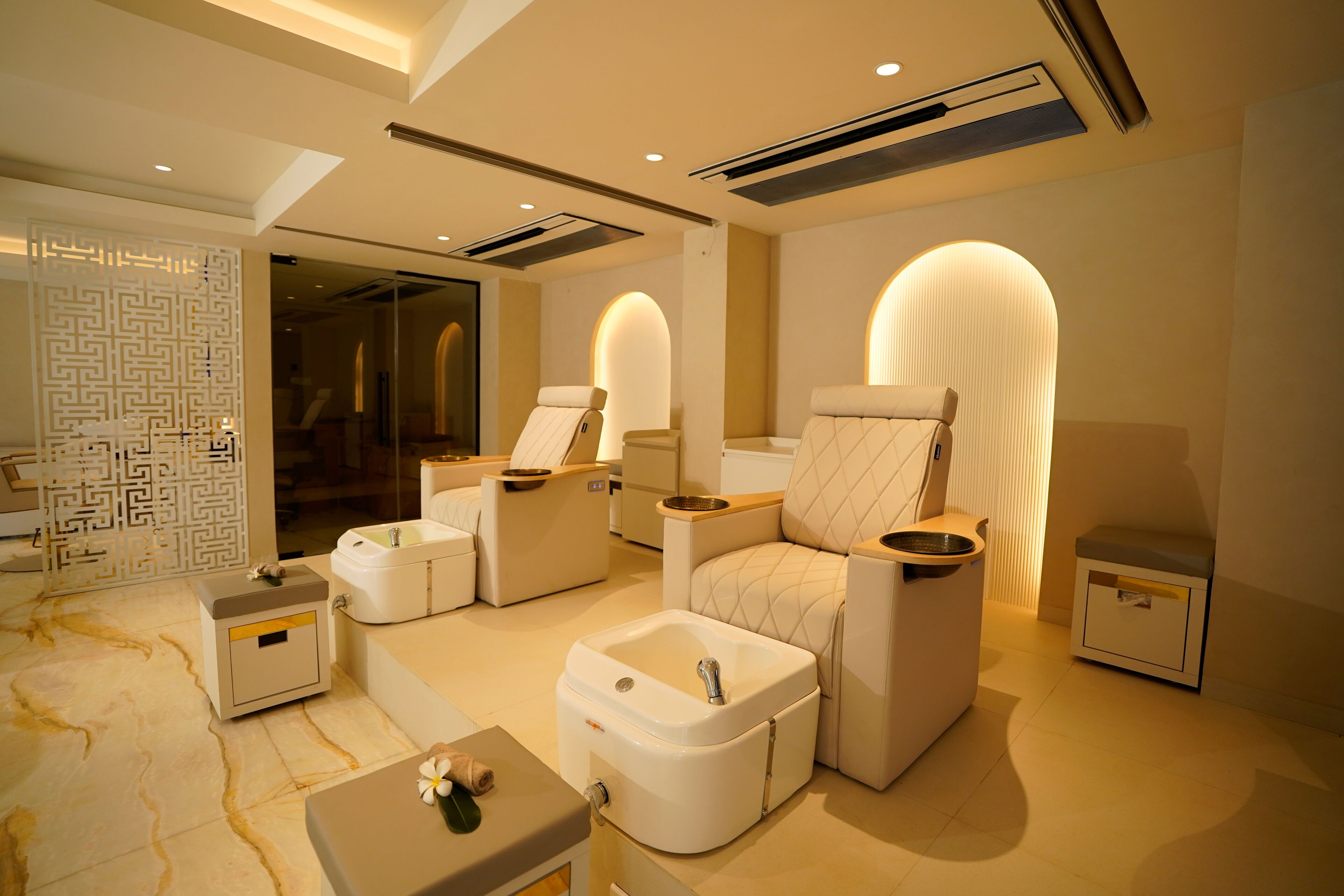 A modern spa room with a massage chair, a small table, a footrest, and a sink.
