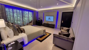 A modern hotel room with a large bed, a sofa, a TV screen, and a desk. - Kings Mansion (Candolim)