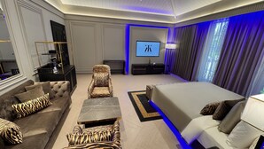 A modern bedroom with a large bed, a sofa, a chair, and a TV. - Kings Mansion (Candolim)