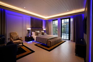 A modern bedroom with a large bed, a zebra-patterned chair, and a view of the outdoors through a large window. - Kings Mansion (Candolim)