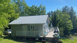 Ein kleines, eingeschossiges Haus mit einer Metalldecke, einer Veranda mit weißen Geländern und einer Terrasse mit Gartenmöbeln.