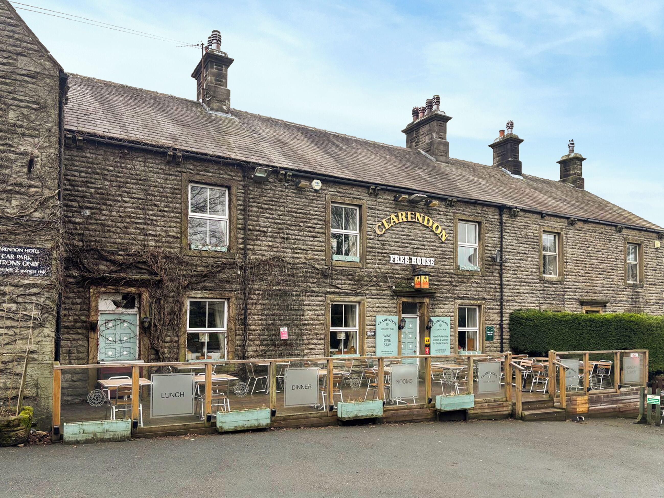 A stone building with a sign reading 'CLEARENDON FREE HOUSE' and multiple signs for 'LUNCH,' 'DINNER,' and 'ROOMS.'