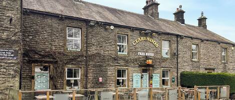 A stone building with a sign reading 'CLEARENDON FREE HOUSE' and multiple signs for 'LUNCH,' 'DINNER,' and 'ROOMS.'