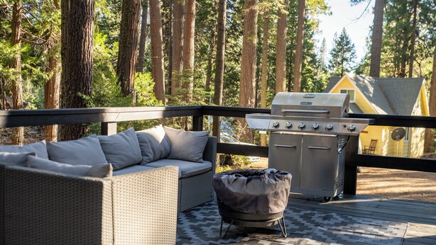 Una terrazza con un divano in vimini, un pouf e un barbecue.