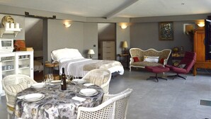 Ein geräumiges Zimmer mit einem Bett, einem Esstisch für zwei Personen und einer Sitzecke mit Sessel und Sofa.
