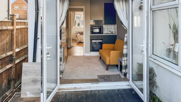 Een modern appartement met keuken, zithoek met een bank, en een slaapkamer zichtbaar door een open deur.