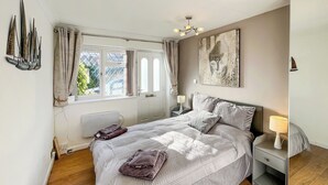 Een slaapkamer met een bed, nachtkastjes, een raam met gordijnen, een radiator, een plafondlamp en een aan de muur hangend kunstwerk.