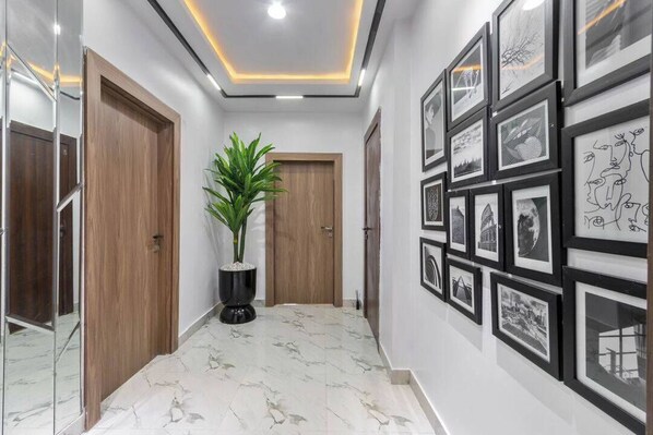 A hallway with a potted plant, framed pictures on the wall, and a marble floor. - Royal Court Apartment (Abuja)