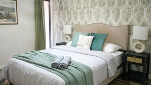 A neatly made bed with a green blanket and rolled towels, two bedside lamps, a headboard, and a patterned wallpaper. - Spacious 3BR Home in Clinton. Weekly & Monthly Discounts Available! (Clinton)