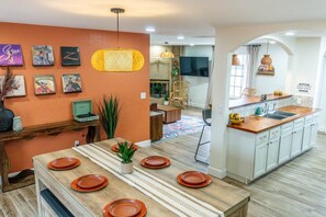 A modern kitchen with a central island, a dining area with a long table, and a living space with a sofa and a TV. - Agave Azul Villa | Monthly/Weekly Discounted Rates (Clinton)