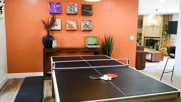 Une table de ping-pong dans une pièce aux murs orange, avec un banc en bois et des tableaux encadrés accrochés au mur.