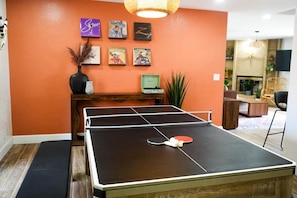 A ping pong table in a room with orange walls, a wooden bench, and framed pictures on the wall.