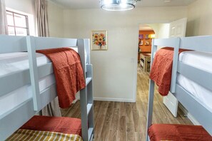 A room with bunk beds, a wooden floor, a painting on the wall, and a door leading to another room. - Agave Azul Villa | Monthly/Weekly Discounted Rates (Clinton)